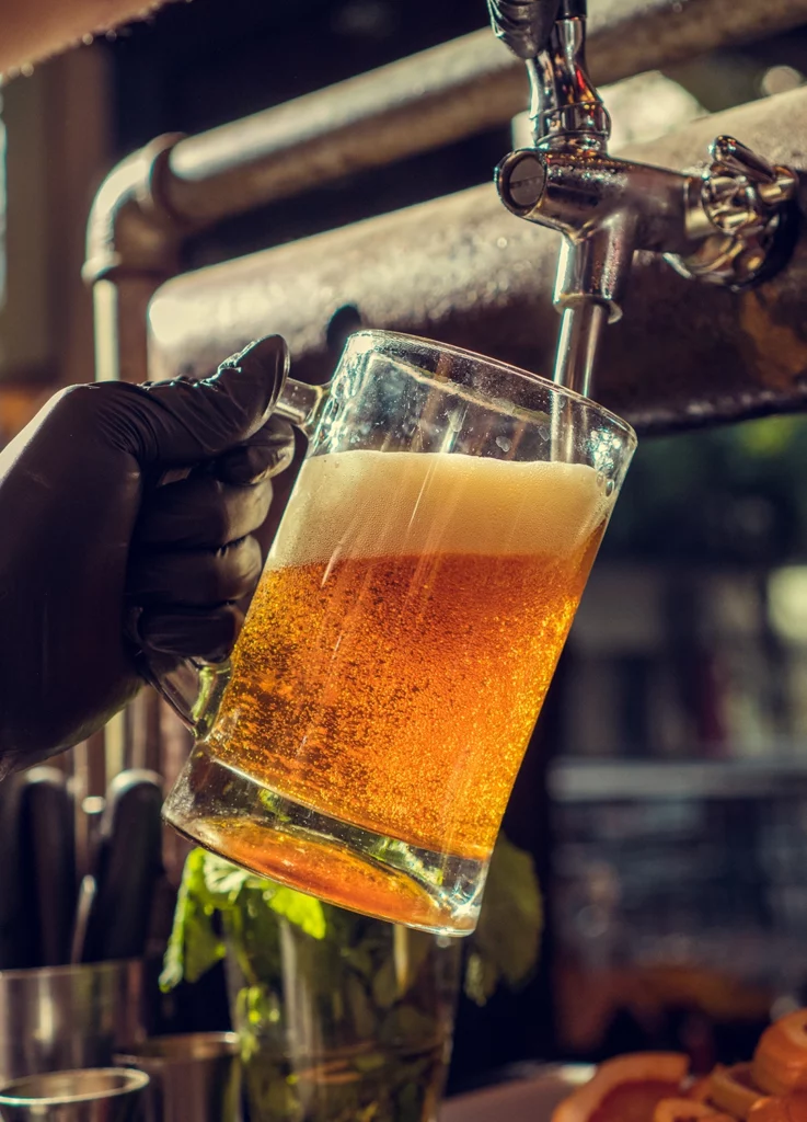 MÜW BEER : chope de bière dorée servie à la pression, mousse épaisse, main gantée au bar.